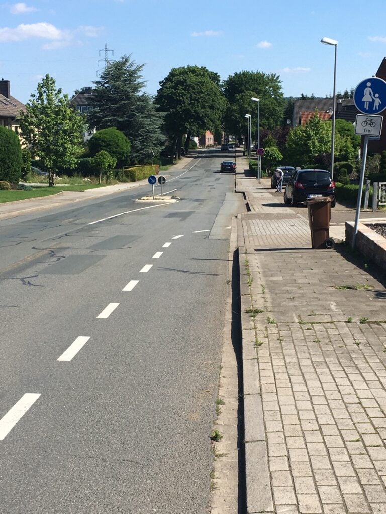 Ein Radstreifen auf der Fahrbahn mündet in einer abgeflachten Einfahrt auf dem Fußweg, der in einem sehr schlechten Zustand ist